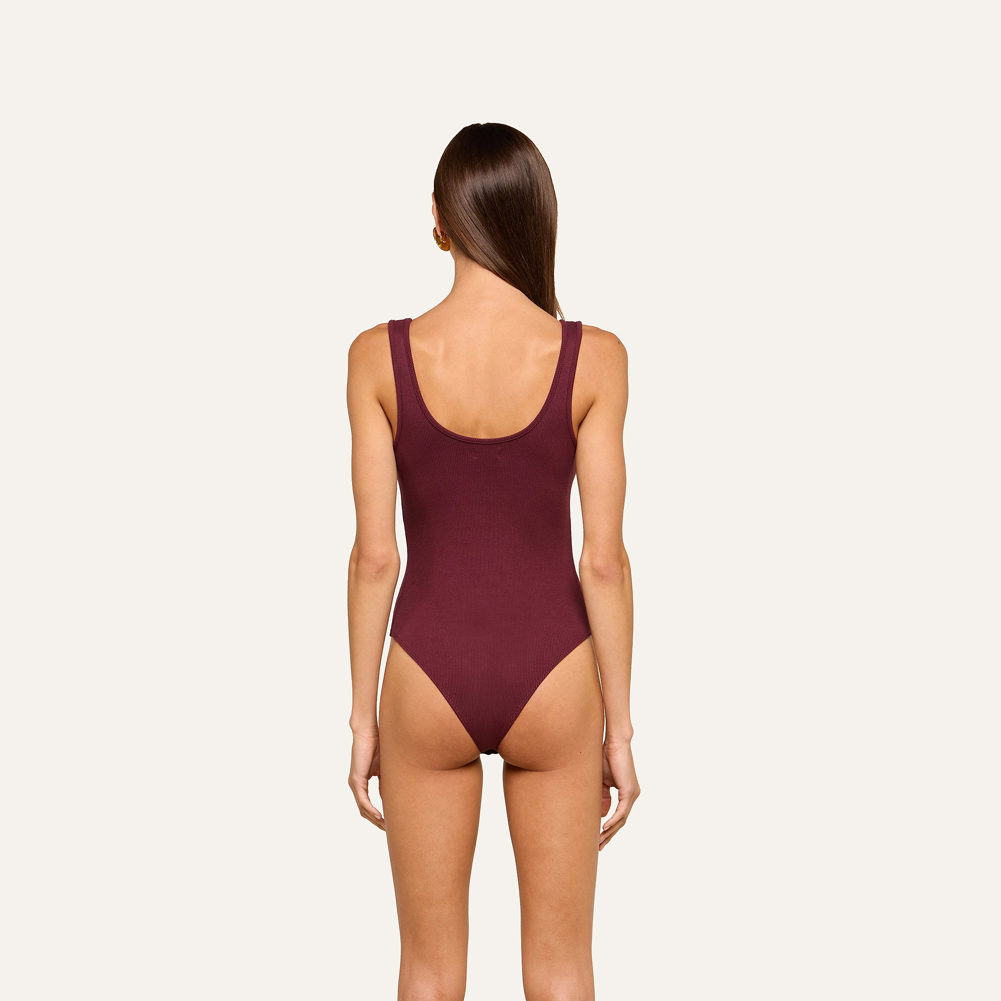 A woman with straight brown hair models the Nica Scoopneck Bodysuit in maroon, featuring high recovery stretch fabric, shown from the back against a plain light background.