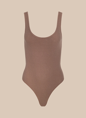 The Nica Scoopneck Bodysuit is a ribbed, sleeveless base layer with a sculpted fit, scoop neckline, and high-cut leg openings. Shown on a plain beige background, it’s ideal for layering with any outfit.