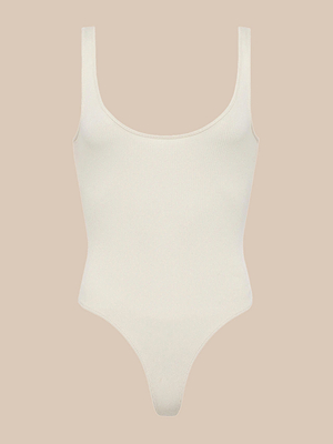 The Nica Scoopneck Bodysuit is a sleeveless, stretch-cotton one-piece with a scoop neckline and high-cut leg openings, shown against a plain beige background.