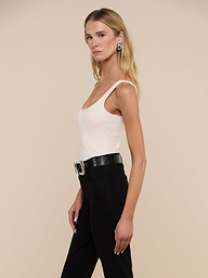 A woman with long blonde hair is wearing the Nica Scoopneck Bodysuit, styled with black pants, a black belt featuring a large buckle, and earrings. She stands against a plain light background, facing left in a relaxed pose.