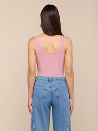 Une personne aux longs cheveux bruns, vêtue dun body rose Nica Scoopneck et dun jean bleu sculpté à taille haute, se tient de face sur un fond beige.