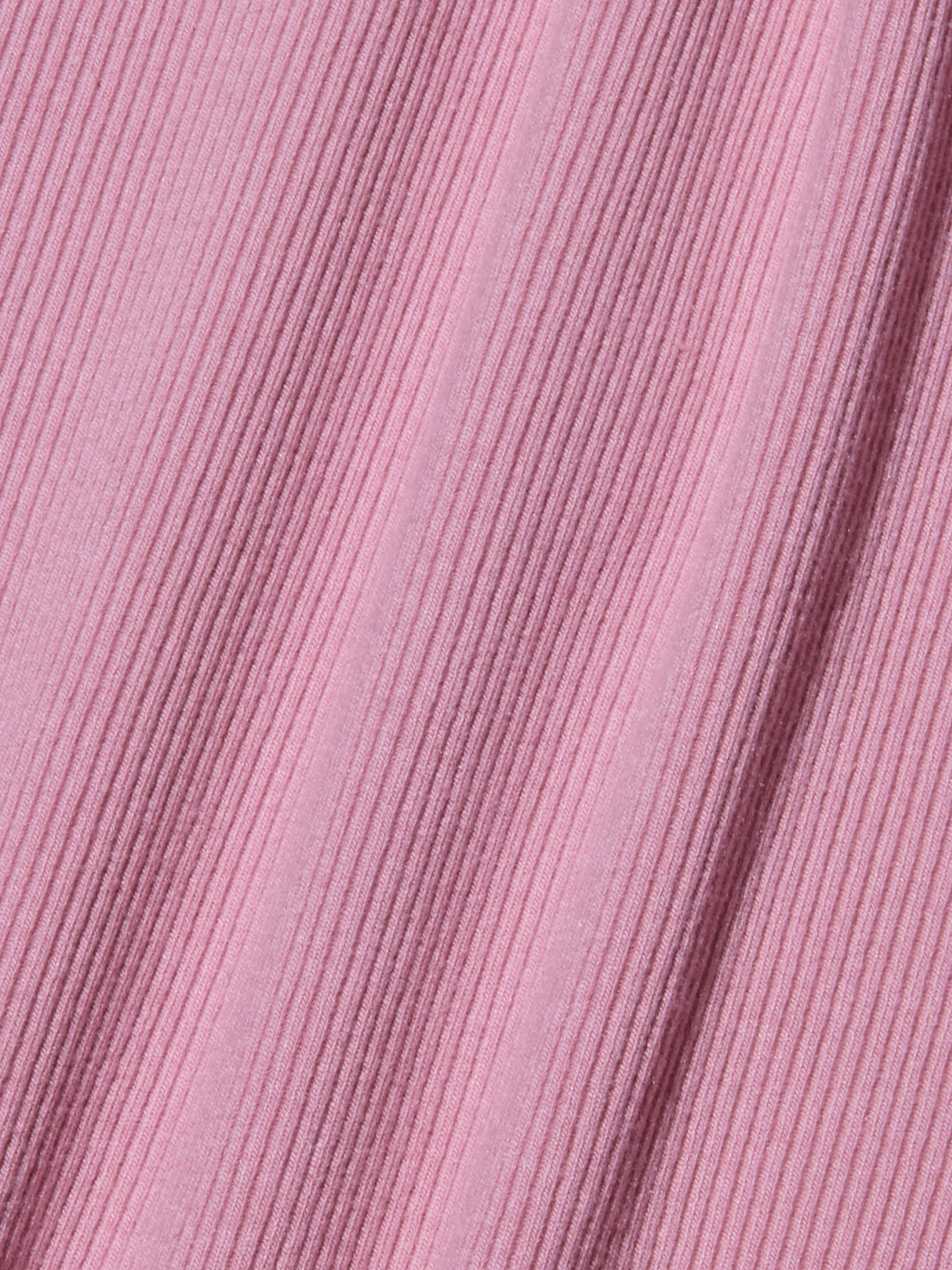 Gros plan sur un tissu côtelé rose avec des lignes texturées diagonales, créant une surface douce et à motifs. Le tissu appartient au body Nica Scoopneck et présente de légères ombres le long des crêtes sculptées de la coupe, là où il est légèrement étiré.