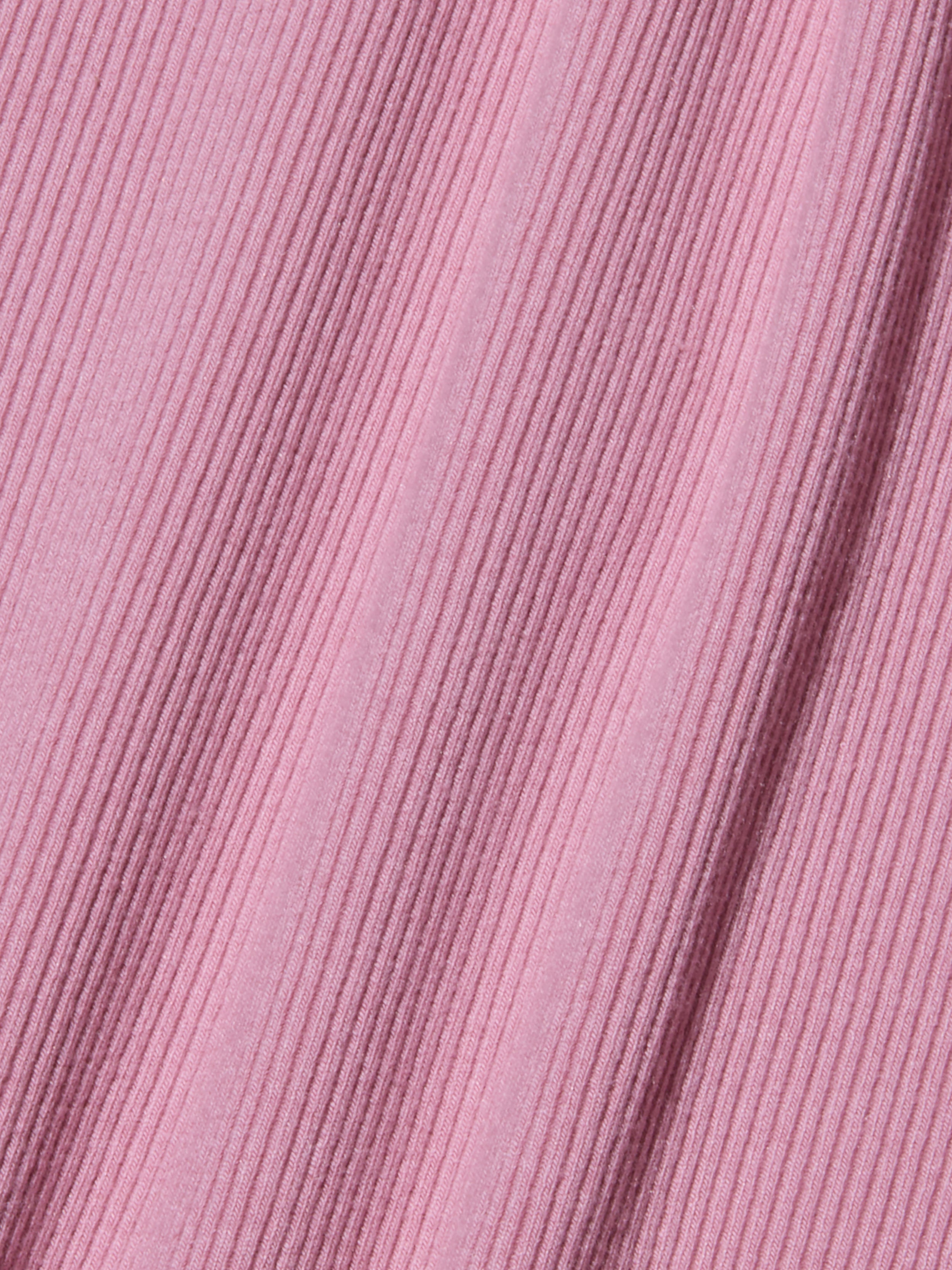 Gros plan sur un tissu côtelé rose avec des lignes texturées diagonales, créant une surface douce et à motifs. Le tissu appartient au body Nica Scoopneck et présente de légères ombres le long des crêtes sculptées de la coupe, là où il est légèrement étiré.