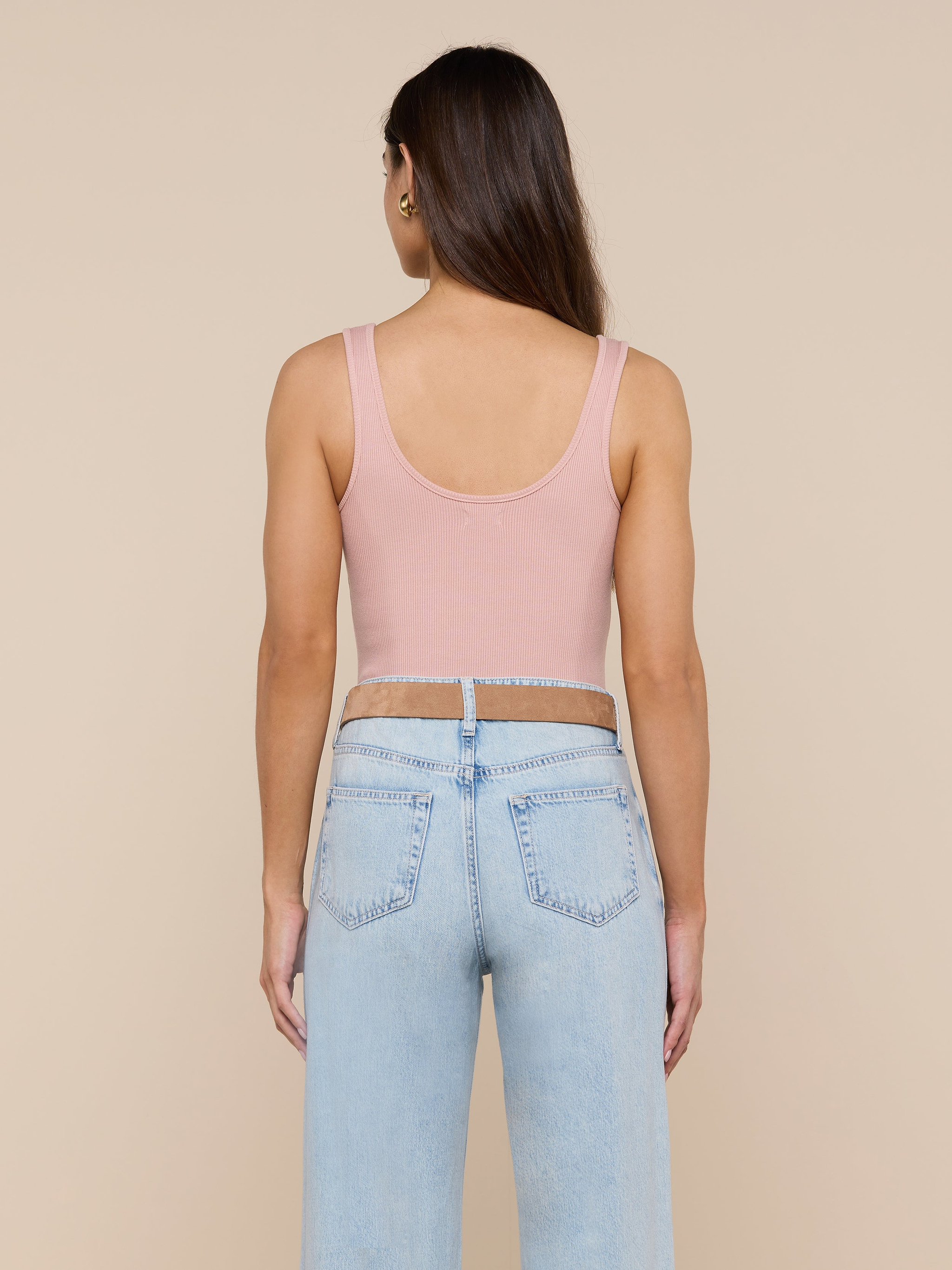 A person with long brown hair is wearing the Nica Scoopneck Bodysuit in pink and light blue sculpted-fit jeans, standing facing away against a plain background.
