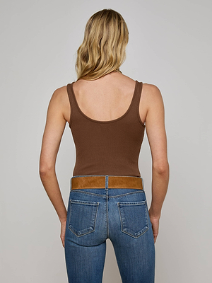 A woman with long blonde hair is shown from the back, wearing a deep brown L'AGENCE Nica Scoopneck Bodysuit and blue jeans with a brown belt, standing against a plain light gray background.