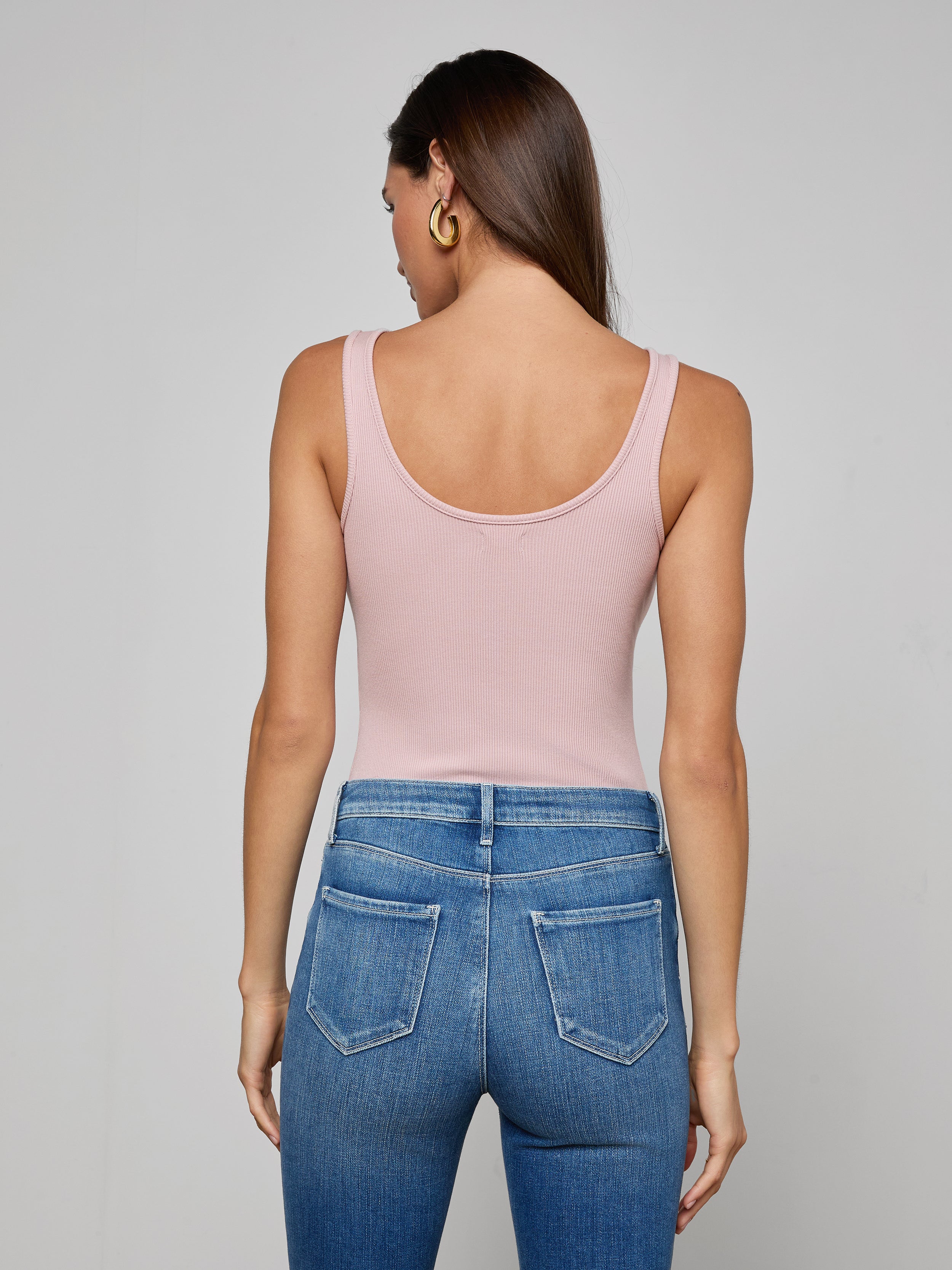 A woman is shown from the back, wearing the Nica Scoopneck Bodysuit in light pink, paired with blue jeans featuring visible back pockets, against a plain light background.