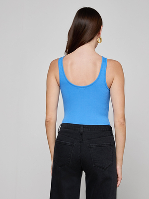 A woman with long brown hair wears the Nica Scoopneck Bodysuit in blue as a base layer, paired with high-waisted black jeans. Seen from the back, she accessorizes with a gold hoop earring against a plain light gray background.