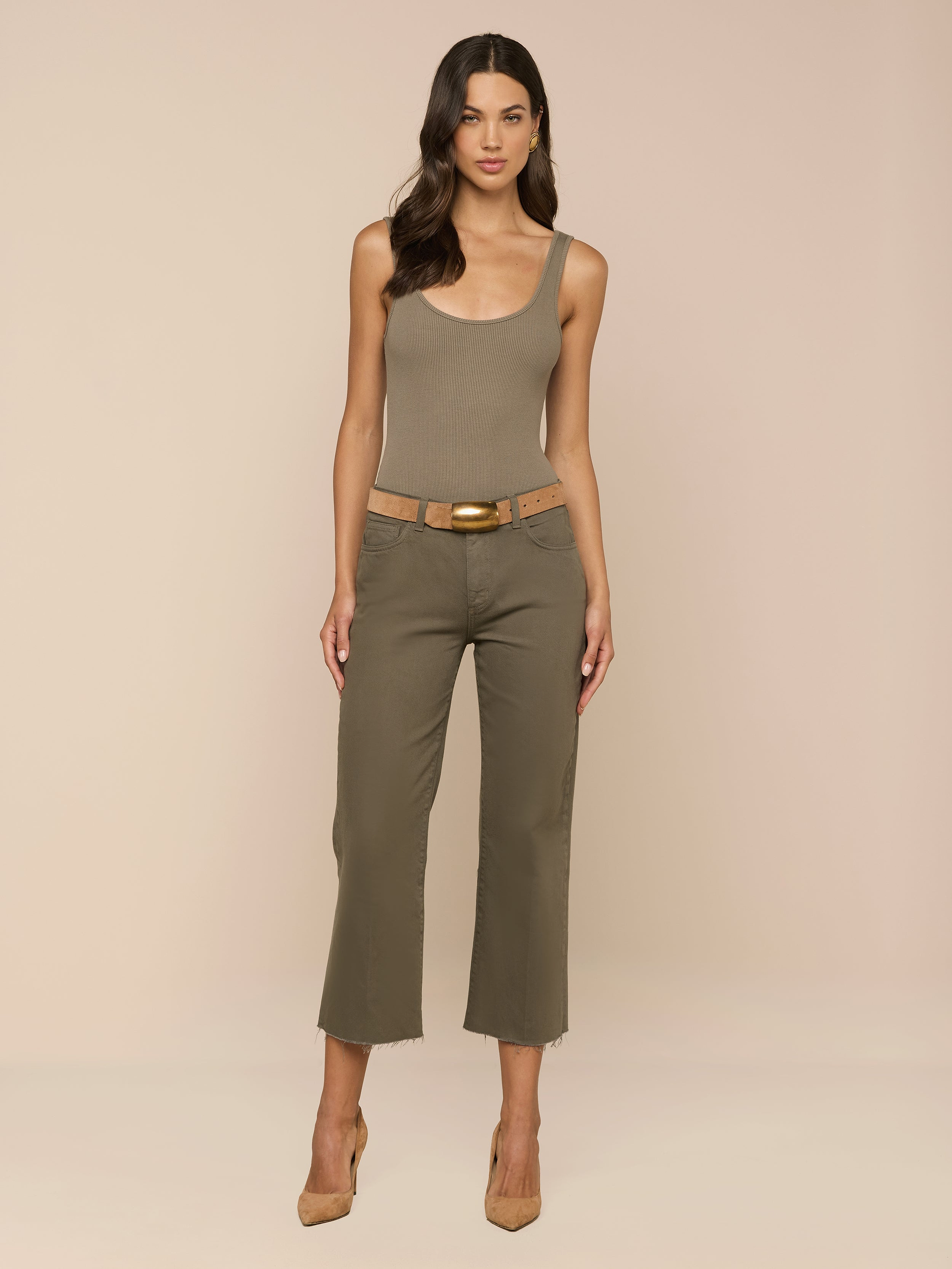 A woman stands facing forward, wearing the Nica Scoopneck Bodysuit in a sculpted fit, olive cropped pants with a tan belt, and tan high heels against a plain light background.