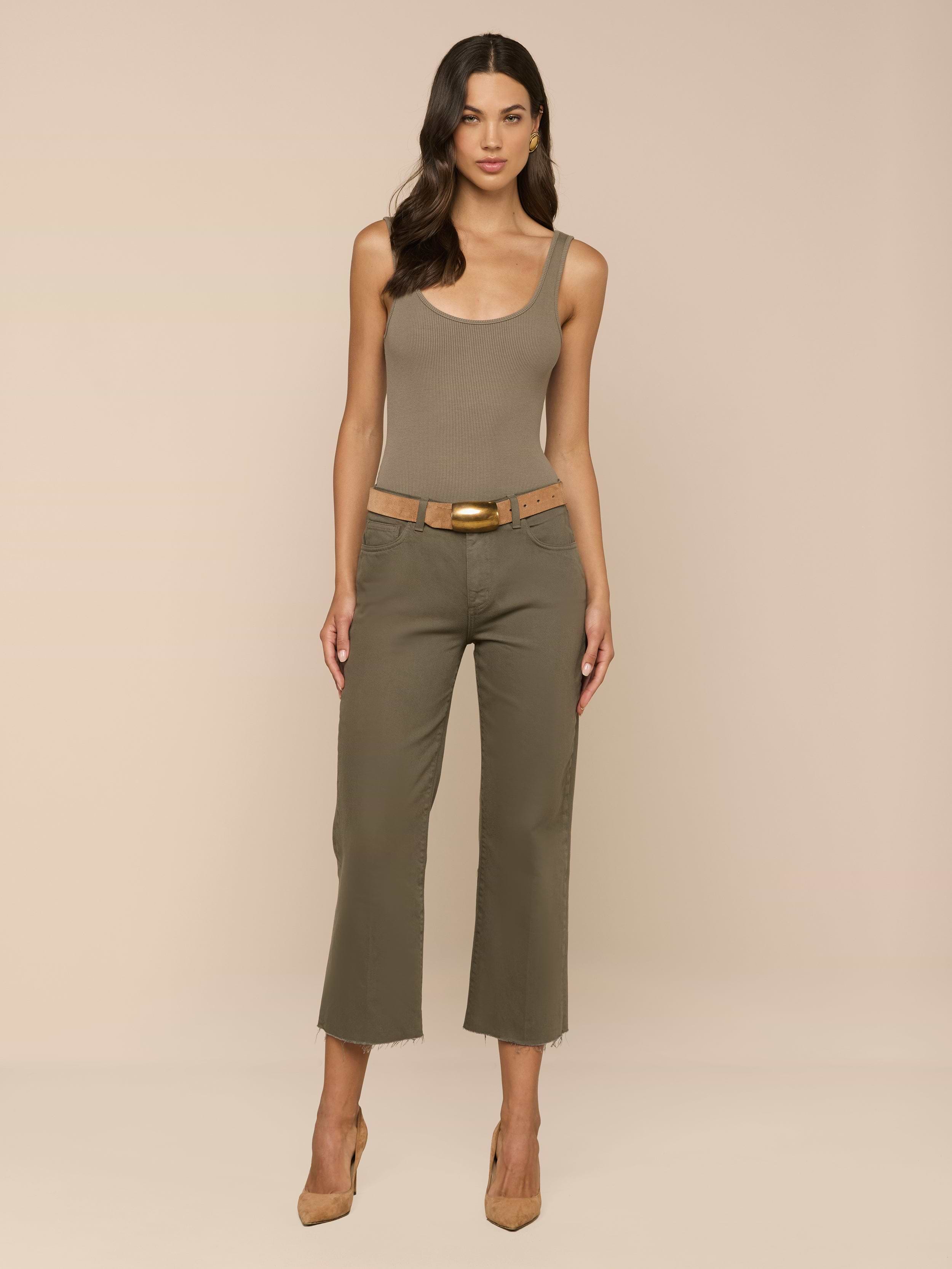 A woman stands facing forward, wearing the Nica Scoopneck Bodysuit in a sculpted fit, olive cropped pants with a tan belt, and tan high heels against a plain light background.