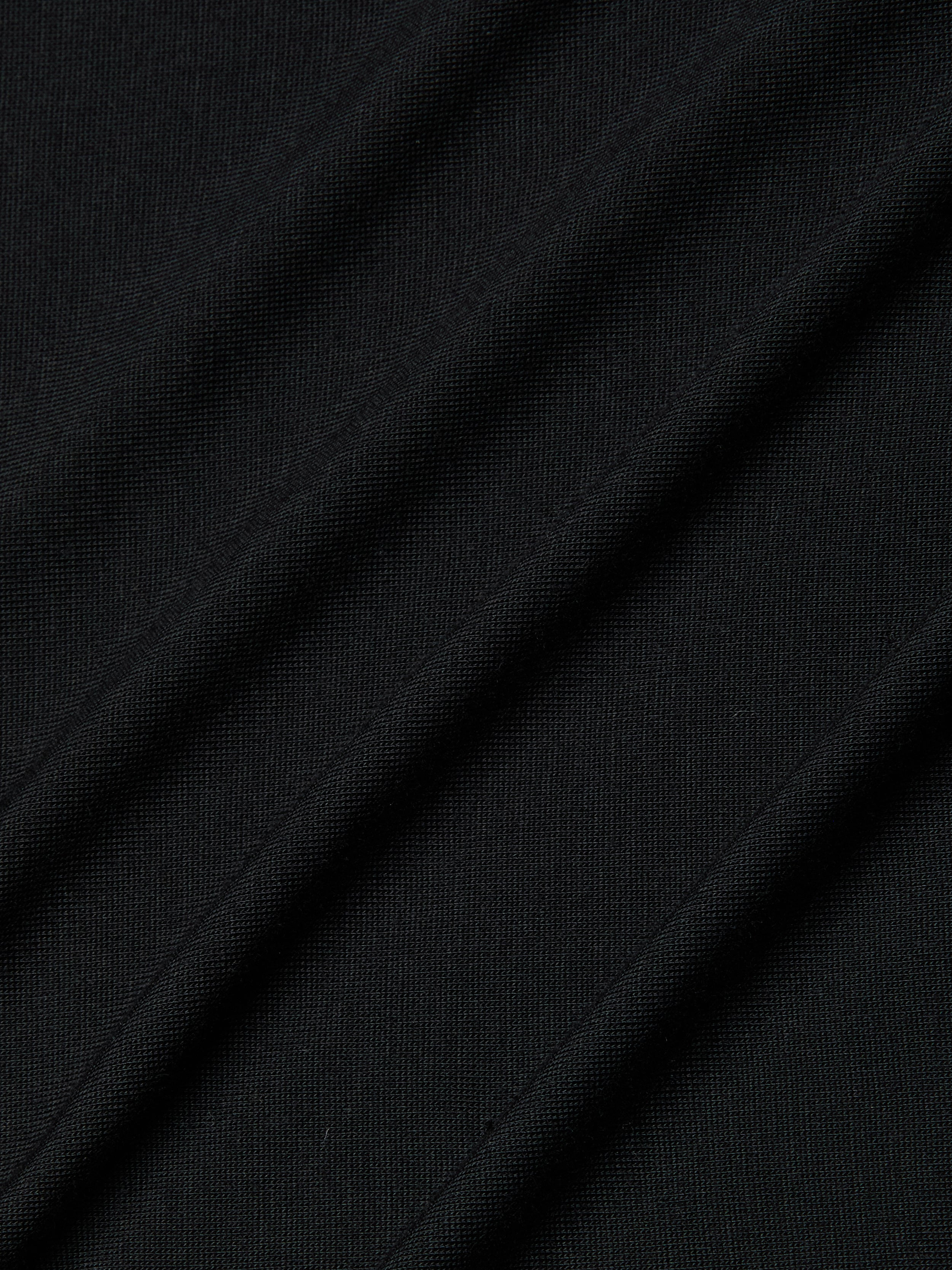 Close-up of the Remy Tee in black micro modal jersey fabric with diagonal folds and visible texture, highlighting its fine knit pattern and subtle shadows for a relaxed fit.