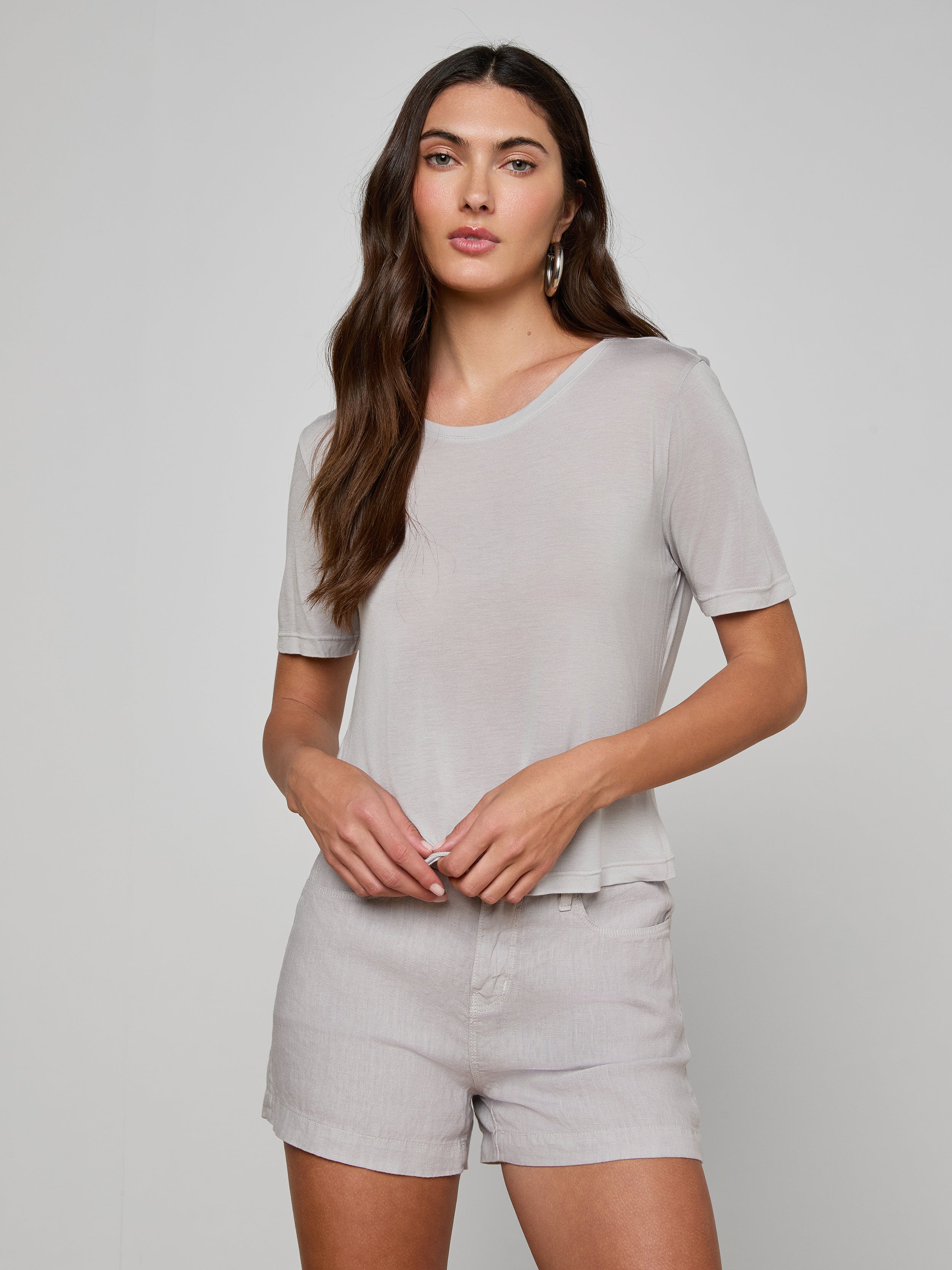 Woman with long brown hair wearing the Remy Tee in light gray, styled with matching shorts, standing against a plain light background.