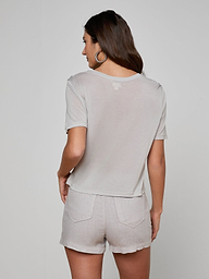 A woman with long brown hair, wearing hoop earrings and the Remy Tee in light gray micro modal jersey with matching relaxed-fit shorts, stands with her back to the camera against a plain white background.