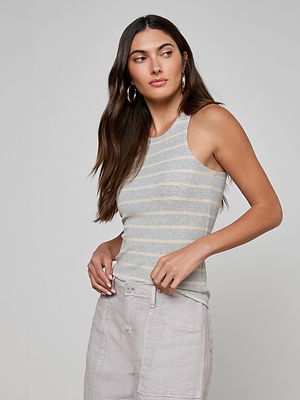 A woman with long brown hair wears the Nia Ribbed Tank—a sleeveless, gray and white striped racerback top made of soft microfiber modal—paired with light pants, standing against a plain light background and looking to her left.