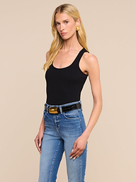 A woman with long blonde hair wears the Adira Scoopneck Tank in black, paired with blue jeans, a black belt with a gold buckle, and gold earrings, standing against a plain light background.