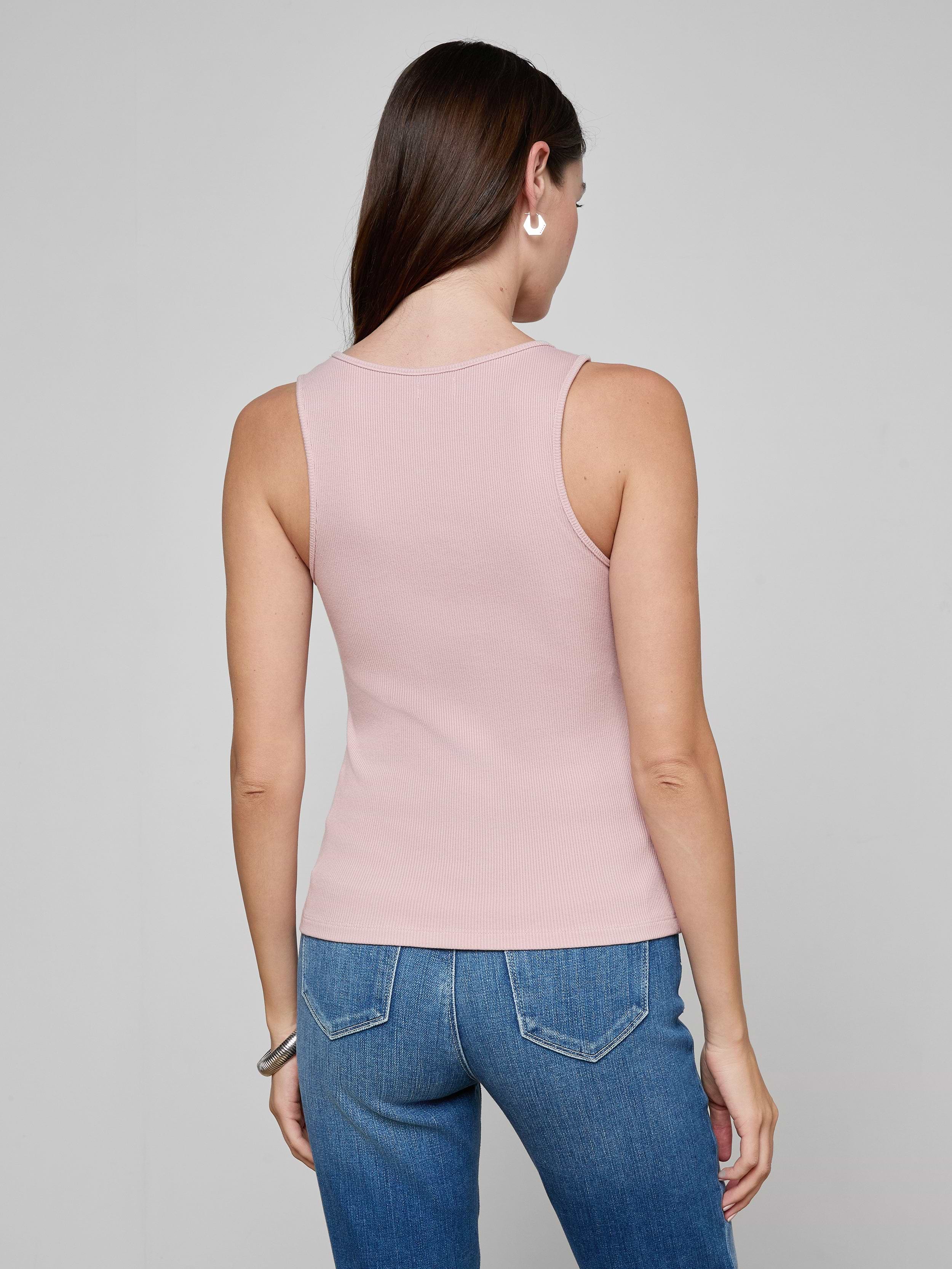 A woman with long brown hair stands facing away, wearing the Adira Scoopneck Tank in light pink and blue jeans against a plain light background.