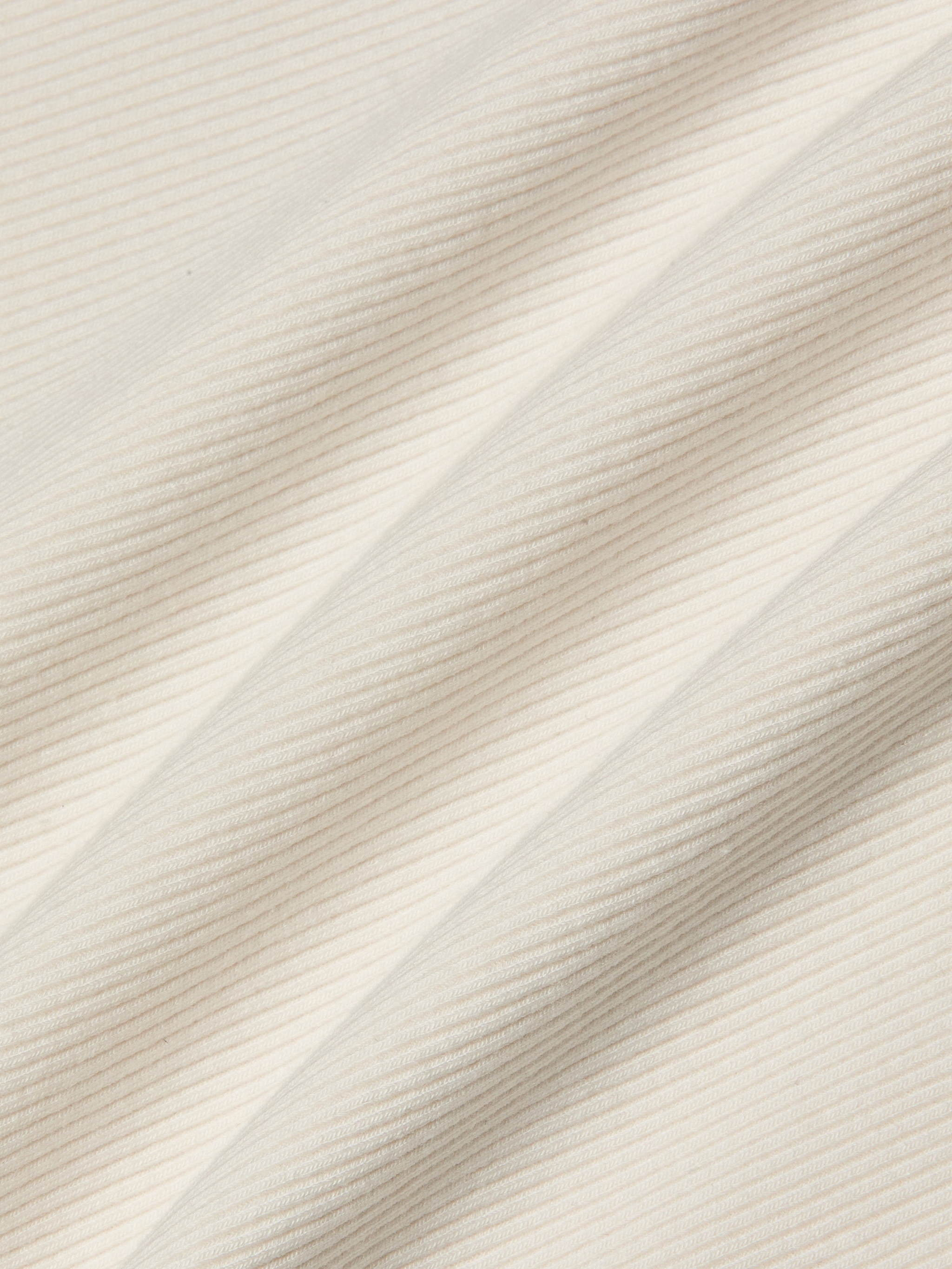 Close-up of the Adira Scoopneck Tank in cream-colored fitted stretch rib fabric, featuring diagonal ridges that form a textured pattern of fine, parallel lines.