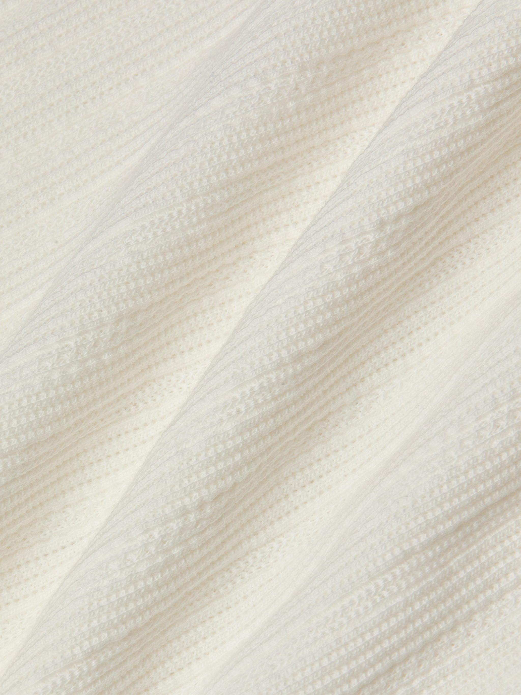 Close-up of the Adira Scoopneck Tank in white ribbed knit cotton pointelle fabric, featuring diagonal lines and textured patterns, with soft folds that create a cozy appearance.