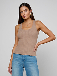 A woman wearing the Adira Scoopneck Tank—a fitted, ribbed beige organic cotton top—paired with blue jeans stands against a plain light background, one hand on her hip and a neutral expression.