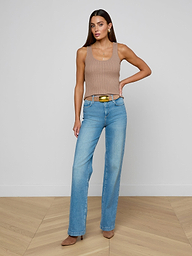 A woman models the Adira Scoopneck Tank— a fitted, sleeveless beige top with a scoop neckline— paired with blue jeans and brown heels, standing with one hand on her hip against a plain white background.