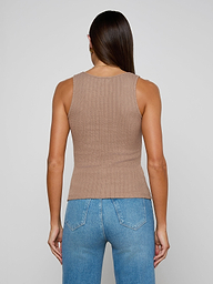 A woman with long brown hair, wearing the Adira Scoopneck Tank—a fitted, sleeveless beige top made from organic cotton—and blue jeans stands with her back to the camera against a plain light background.