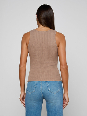 A woman with straight, dark brown hair stands with her back to the camera, wearing the Adira Scoopneck Tank in beige and light blue jeans. The background is plain and light-colored.