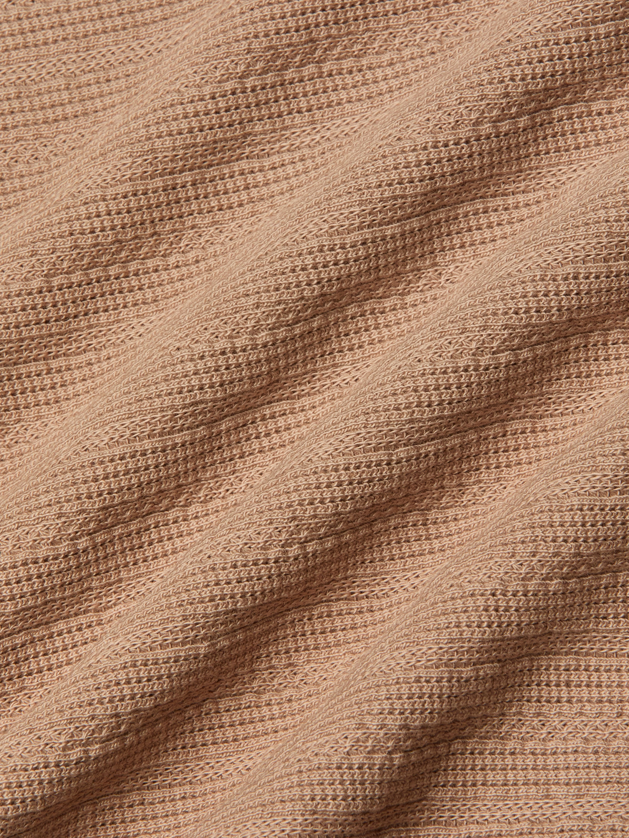 Close-up of the Adira Scoopneck Tank in peach-colored organic cotton, featuring a ribbed, textured pattern in diagonal lines. The soft material is slightly stretched, highlighting the details of the individual knit stitches.