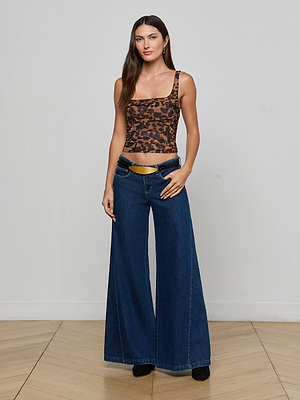 Against a plain background, a woman wears the L'AGENCE Rasha Shirred Mesh Tank and wide-leg blue jeans, her thumbs hooked in the waistband and her hair down.
