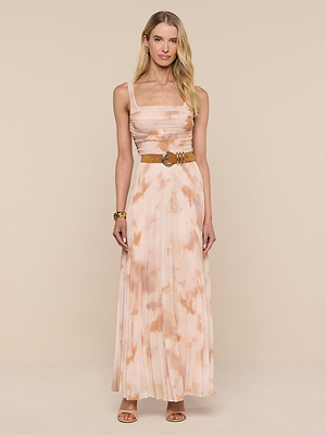 A woman poses against a beige background in the Rasha Shirred Mesh Tank, a sleeveless, pleated, peach and white abstract print dress with a tan belt and heeled sandals. She has long, wavy blonde hair and gold accessories.