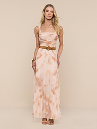 A woman stands against a white background wearing the Rasha Shirred Mesh Tank styled as a long, sleeveless dress with an abstract light pink and beige print, paired with a belt and heeled sandals.