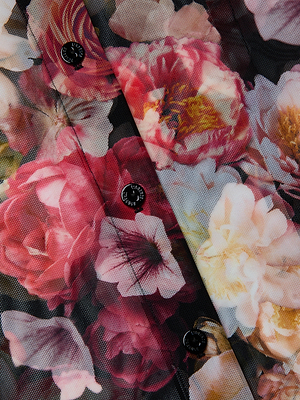 Close-up of the Indiana Mesh Blouse by L'AGENCE—a sheer button-down top with a colorful rose floral print in pink, red, yellow, and cream hues, featuring sleek black buttons down the center.