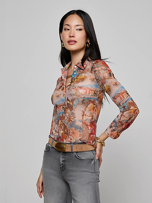 A woman with long black hair poses against a plain background, wearing the Indiana Mesh Blouse by L'AGENCE styled with a light brown belt, gray jeans, and gold jewelry.