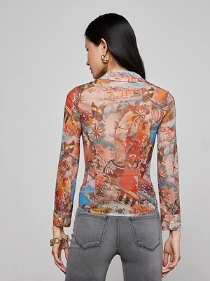 A woman with long dark hair, wearing gold hoop earrings and the colorful Indiana Mesh Blouse by L'AGENCE, stands facing away from the camera in gray jeans against a plain gray background.