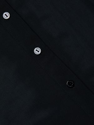 Close-up of the Indiana Mesh Blouse: a black fitted top with diagonal stitching and three buttons—two light, one dark—all inscribed with SAVAGE.