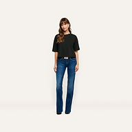 A woman wears a black relaxed-fit Daria Oversized Cropped Tee made of Supima cotton with blue bootcut jeans and a belt.