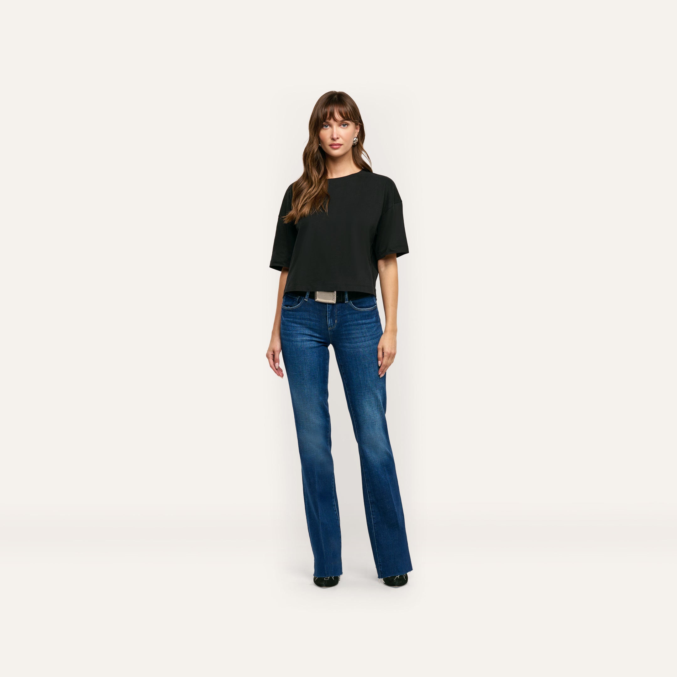 A person wearing a black, relaxed fit Daria Oversized Cropped Tee in Supima cotton paired with blue flared jeans.