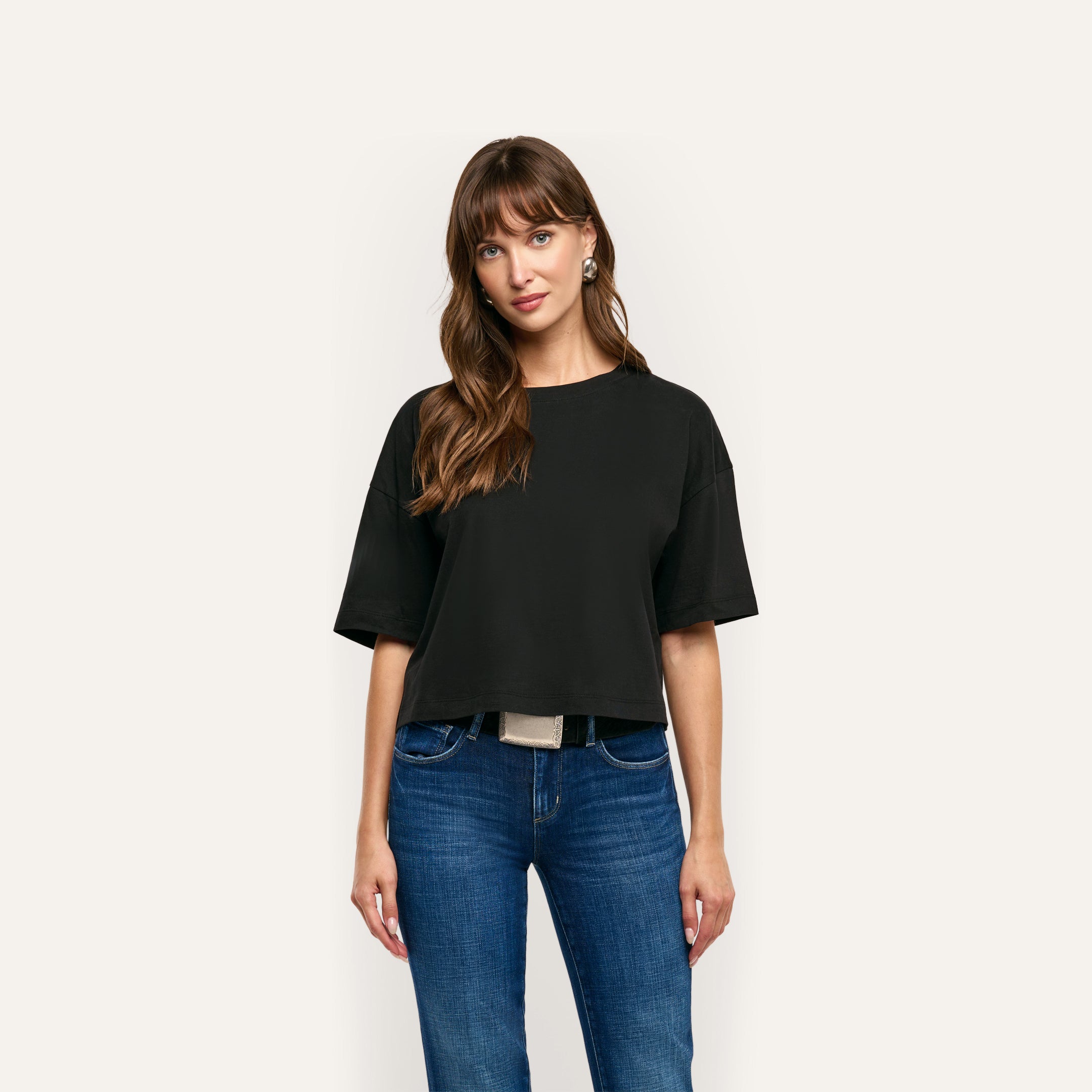 A person wearing a plain, black, oversized cropped Daria Oversized Cropped Tee made of Supima cotton with a relaxed fit and blue jeans.