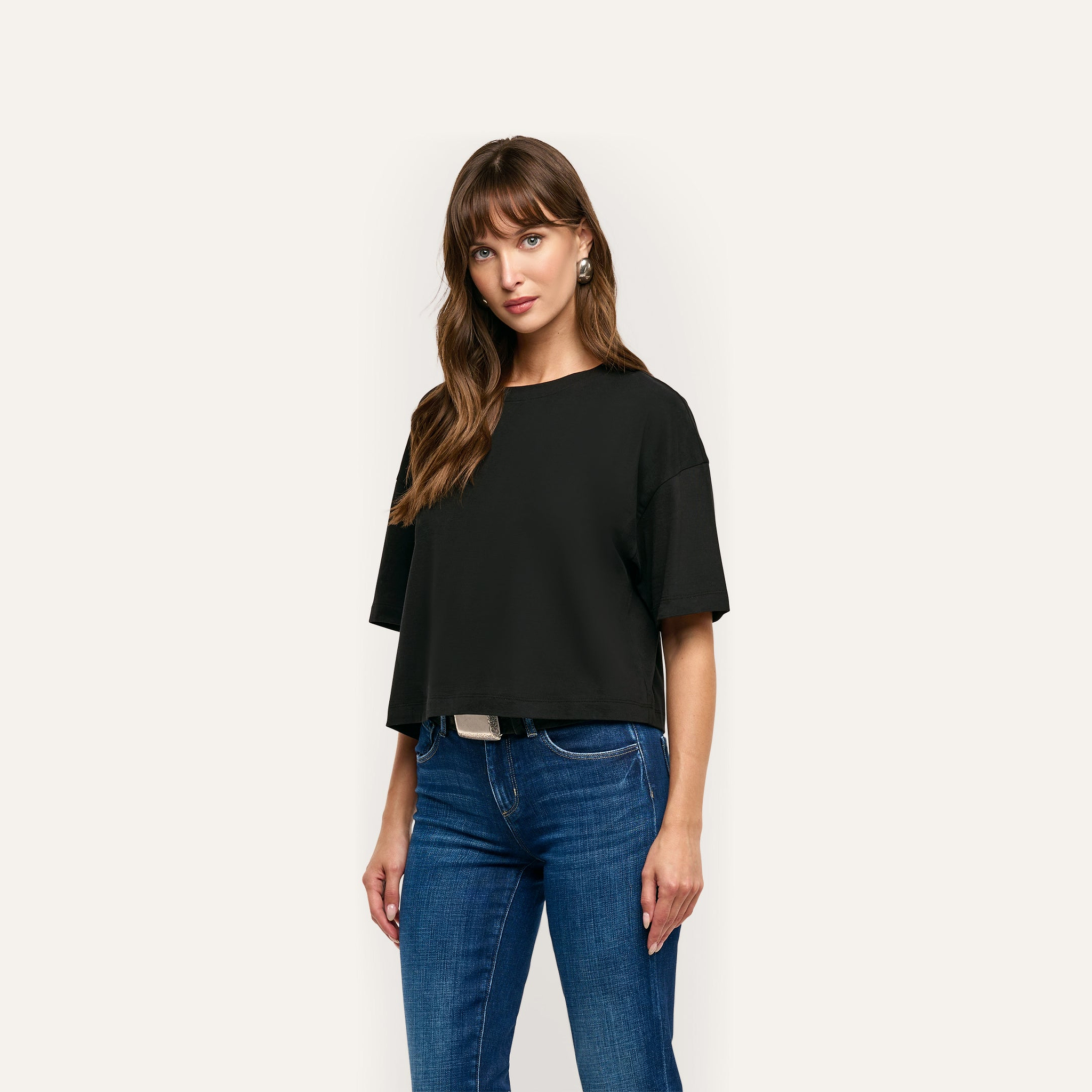 A person wearing a relaxed fit, oversized black Daria Oversized Cropped Tee made of Supima cotton and blue jeans.