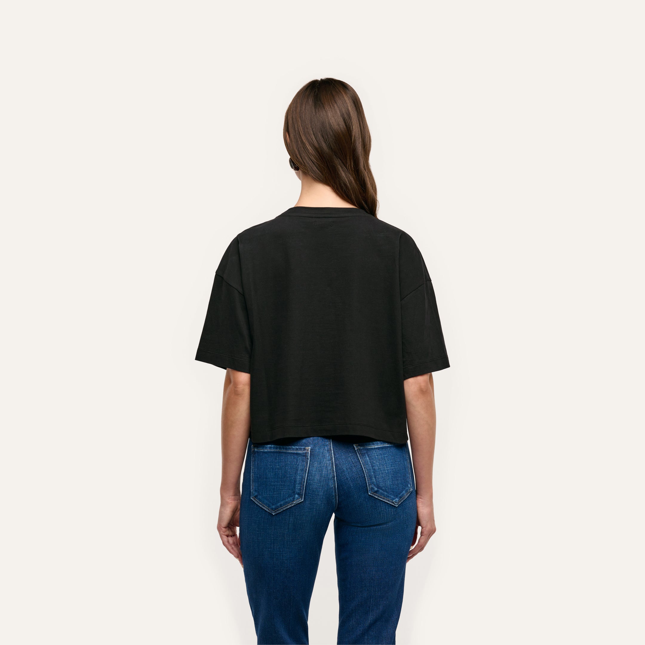 Back view of a person wearing a black Daria Oversized Cropped Tee made of Supima cotton and relaxed-fit blue jeans.