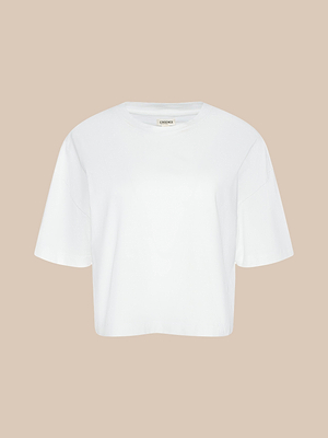 Das „Daria Oversized Cropped Tee“, ein schlichtes weißes Kurzarm-T-Shirt in Oversize-Passform, wird vor einem beigen Hintergrund präsentiert.