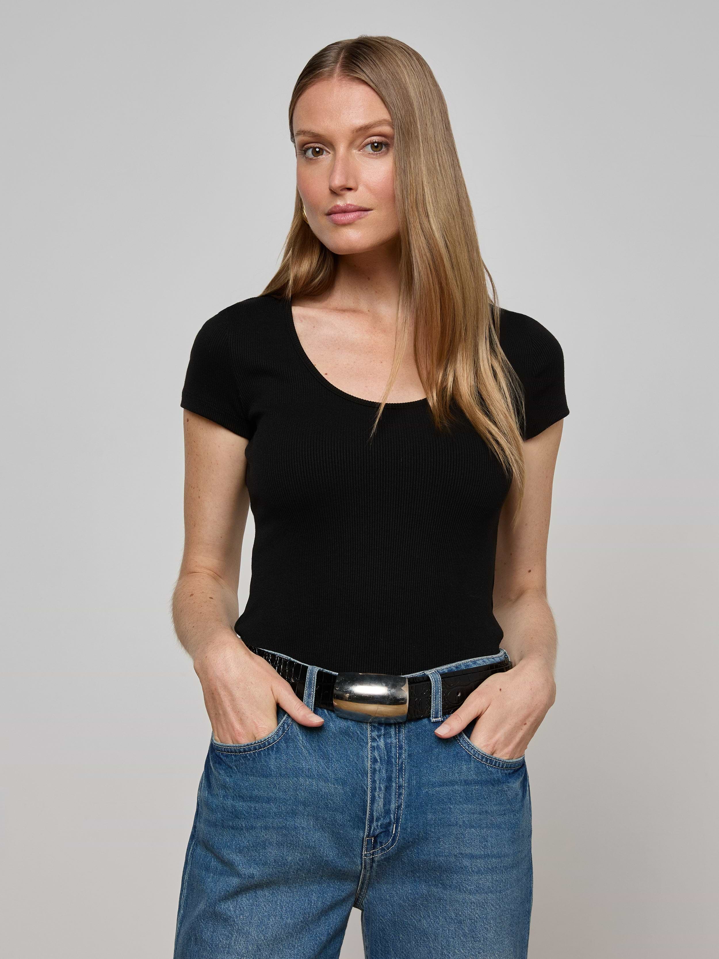A woman with long, straight blonde hair wears the Brynlee Scoopneck Tee in black and blue jeans, standing with her hands in her pockets against a plain light background.