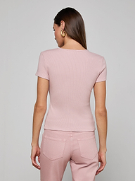 A woman with long brown hair and gold hoop earrings wears the Brynlee Scoopneck Tee in light pink and pink denim jeans, standing with her back to the camera against a plain light background.