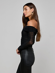 A woman in profile wearing the Poppie Off-The-Shoulder Bodysuit—with stretch mesh sleeves—paired with black fitted pants, standing against a plain, light background.