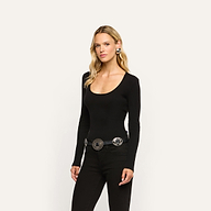 A woman wearing a long-sleeved black Elara Scoopneck Bodysuit in stretch cotton and black jeans with a statement silver concho belt.