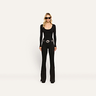 A woman wearing a black Elara Scoopneck Bodysuit, black flared jeans with a large silver statement belt, and dark sunglasses.