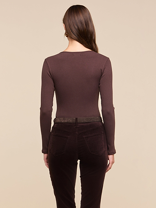 A woman with long brown hair stands facing away, wearing the Elara Scoopneck Bodysuit and dark brown pants against a plain beige background.