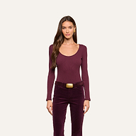 Woman with long brown hair, wearing the Elara Scoopneck Bodysuit—a fitted long-sleeve burgundy top crafted from stretch cotton modal—and high-waisted burgundy pants with a large rectangular belt, stands facing forward against a plain light background.