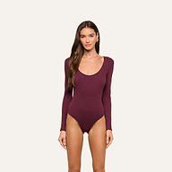 A woman with long brown hair is wearing the Elara Scoopneck Bodysuit in deep burgundy, which features a body-contouring fit made from stretch cotton modal. She is standing against a plain, light background and looking straight at the camera with a neutral expression.