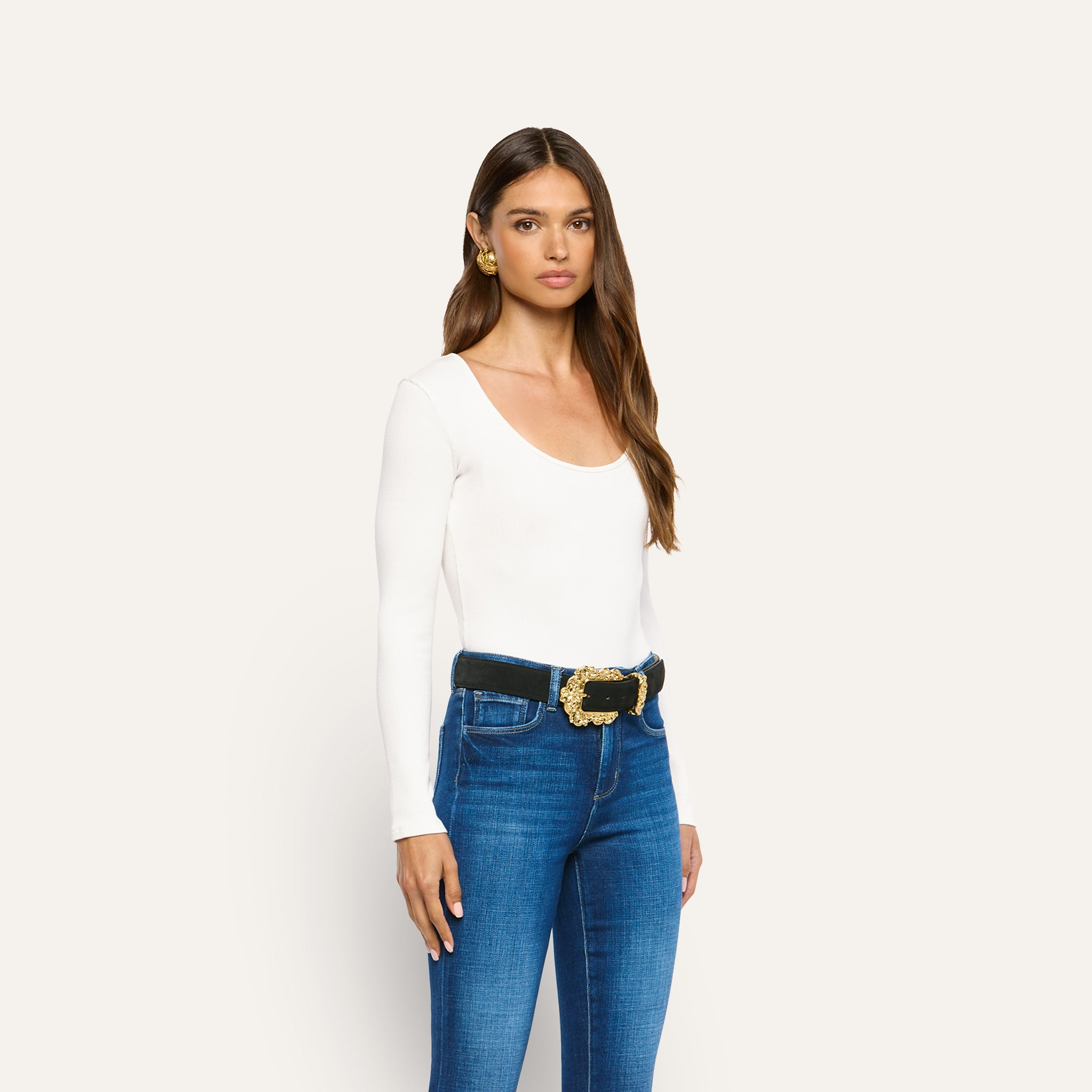A person wearing an Elara Scoopneck Bodysuit tucked into blue jeans with a black belt featuring an ornate gold buckle.