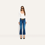 A woman wearing an Elara Scoopneck Bodysuit in white, dark blue cropped flare jeans, a black belt with an ornate gold buckle, and black heels.