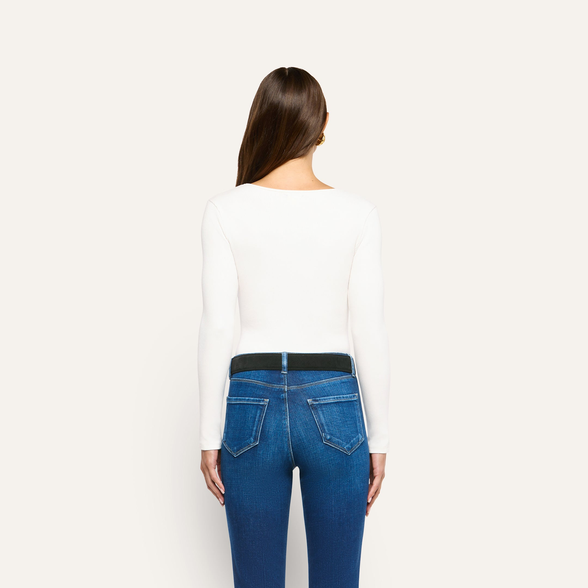 Back view of a person wearing an Elara Scoopneck Bodysuit in stretch cotton tucked into blue jeans with a black belt.